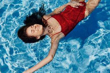 Havuzda yüzen kırmızı mayo giymiş, suda uzanan ve havuzda yüzen güzel bir gülümsemesi olan genç bir kadın. Tatilde dinlenme kavramı. Yüksek kalite fotoğraf