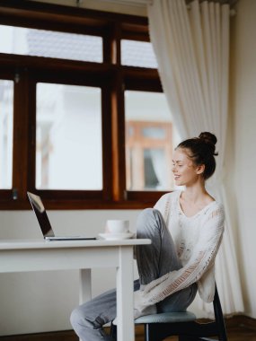 Evde rahat bir yerde, bir bardak içkiyle masa başında çalışan yaratıcı genç bir kadın. İnternette gülümsemesi, iletişimi ve eğitimi olan bir ofis çalışanı. Yüksek kalite fotoğraf