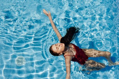 Havuzda kırmızı mayo giyen, suda yatan ve mavi havuzda yüzen güzel bir gülümsemesi olan genç bir kadın. Tatilde dinlenme kavramı. Yüksek kalite fotoğraf