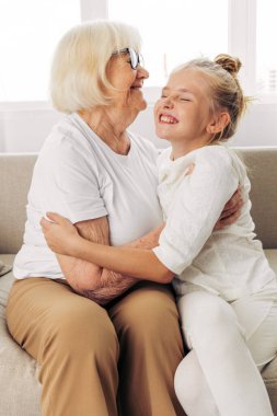 Kadın kanepe kıdemli büyükanne toruna sarılıyor kız kıza sarılıyor aile kızına mutlu, yaşlı anne tarzı çocuk kanepede yatıyor.