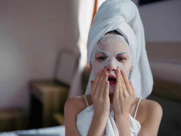 年轻女人躺在床上 洗完澡 脸上戴着保湿美容面罩 头上戴着白毛巾 生活方式家居护肤 面带微笑 高质量的照片 — 图库照片