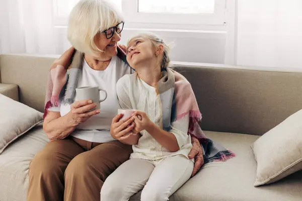 女性のおばあちゃん抱擁ガール 冬の家 平らなマグカップ ソファ 幸せな愛 ライフスタイル ソファー — ストック写真