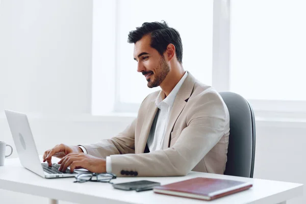 Typing man sitting office laptop using smiling indoors desk computer communication business handsome winner happy confident success online businessman job executive white career