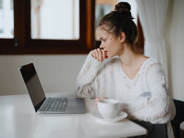 Evde rahat bir yerde, bir bardak içkiyle masa başında çalışan yaratıcı genç bir kadın. İnternette gülümsemesi, iletişimi ve eğitimi olan bir ofis çalışanı. Yüksek kalite fotoğraf