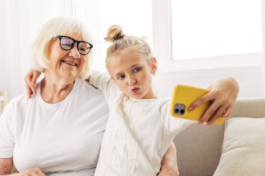 Uzay kucaklaşması beyaz selfie fotokopi eğitimi büyükanne tişörtü kanepeyi arayın birlikte çekilmiş iki aile fotoğrafçılığı gülümseyen torun ev halkına mutluluğu telefon eder.