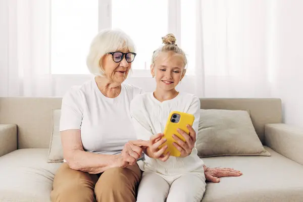 People sofa call grandmother photography togetherness copy t-shirt child adult phone senior bonding two selfie happiness indoors granddaughter hugging family smiling video space education white