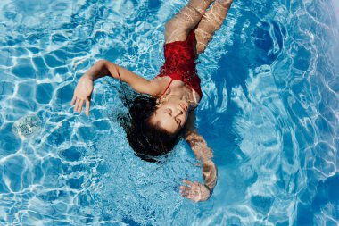 Havuzda kırmızı mayo giyen, suda yatan ve mavi havuzda yüzen güzel bir gülümsemesi olan genç bir kadın. Tatilde dinlenme kavramı. Yüksek kalite fotoğraf