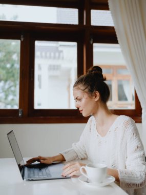 Evde rahat bir yerde, bir bardak içkiyle masa başında çalışan yaratıcı genç bir kadın. İnternette gülümsemesi, iletişimi ve eğitimi olan bir ofis çalışanı. Yüksek kalite fotoğraf