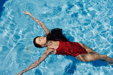 Havuzda yüzen kırmızı mayo giymiş, suda uzanan ve havuzda yüzen güzel bir gülümsemesi olan genç bir kadın. Tatilde dinlenme kavramı. Yüksek kalite fotoğraf