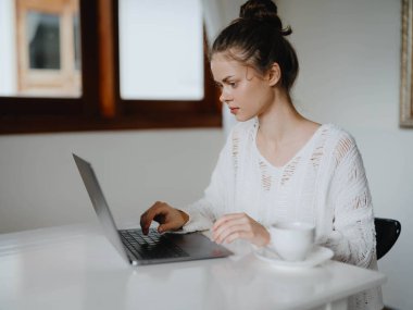 Evde rahat bir yerde, bir bardak içkiyle masa başında çalışan yaratıcı genç bir kadın. İnternette gülümsemesi, iletişimi ve eğitimi olan bir ofis çalışanı. Yüksek kalite fotoğraf