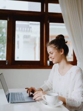 Evde rahat bir yerde, bir bardak içkiyle masa başında çalışan yaratıcı genç bir kadın. İnternette gülümsemesi, iletişimi ve eğitimi olan bir ofis çalışanı. Yüksek kalite fotoğraf