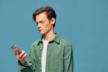 Genç Adam Mavi Arkaplan Karşısında Akıllı Telefonla Mesajlaşıyor