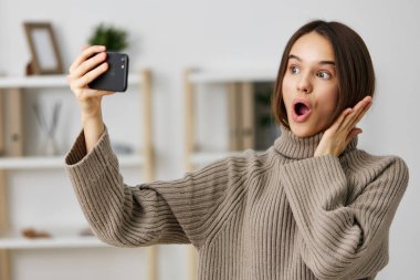 Kameralı kadın Kafkasyalı akıllı telefonlu kadın mobil ev telefonlu güzellik evi, duygusal iç mekan eğlenceli fotoğraf selfie genç blogger moda oda blogu