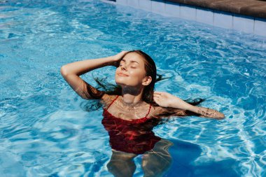 Kırmızı mayo içinde yüzen mutlu bir kadın, güneş ışığında uzun saçlar, güneş kremi ile cilt koruması, tropikal iklimde tatilde dinlenme kavramı. Yüksek kalite fotoğraf