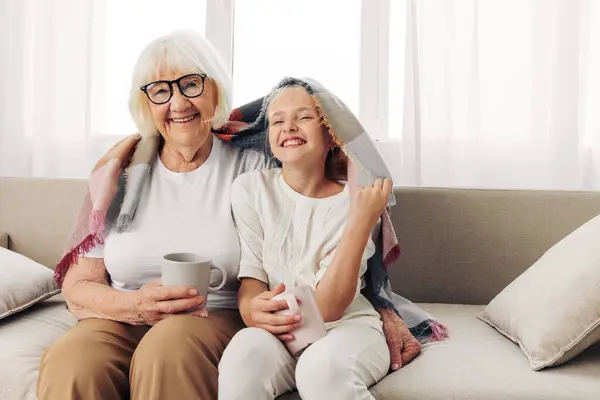 Woman granddaughter winter home love grandmother child happy couch girl plaid family hugging hug elderly old mugs sofa