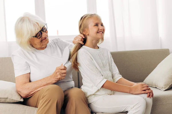 Girl woman couch love old mother elderly child family lifestyle grandmother combing comb hug sofa home hair hair granddaughter happy