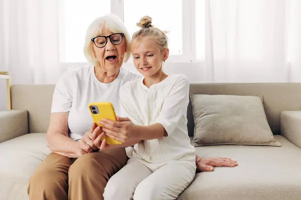 Sofa smiling selfie hugging child phone togetherness granddaughter space grandmother education bonding copy family white call t-shirt photography people two video indoors