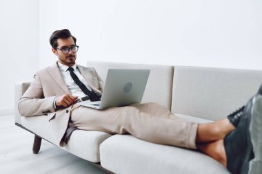 Erkek kanepe mutlu iş koltuğu daire başarı bilgisayar beyaz erkek kapalı alanda çekici gülümseyen video internetteki dizüstü bilgisayar iletişim gevşetilmiş ev idaresi.