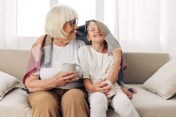 女性シニア抱擁 冬の古いソファー ホーム ソファー マグカップ 平凡な娘 幸せな祖母 ライフスタイル — ストック写真