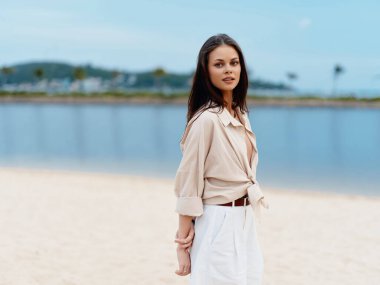 Okyanus Güzeli: Bir Stil ve Çekici Genç Bayan Sahilde Yaz Tatili Yapıyor, Mavi Su ve Güneş Işığı Kıyı şeridine Karşı Mutlu ve Rahat Görünüyor.