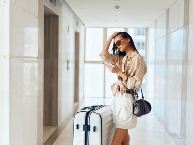 Bavulu ve bavulu olan kadın yolcu havaalanı terminalinden ayrılmaya hazır.