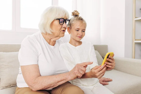 Selfie photography child family t-shirt sofa two white granddaughter phone call indoors smiling togetherness copy video bonding space people happiness grandmother education hugging