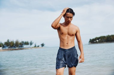 Tropikal Sıçrama: Gülümseyen Asyalı Adam Mavi Okyanusta Özgürlüğü Kucaklıyor, Aktif Bir Yaz Yüzüşünün tadını Çıkartıyor