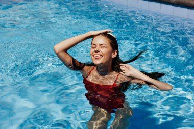 Kırmızı mayo içinde yüzen mutlu bir kadın, güneş ışığında uzun saçlar, güneş kremi ile cilt koruması, tropikal iklimde tatilde dinlenme kavramı. Yüksek kalite fotoğraf