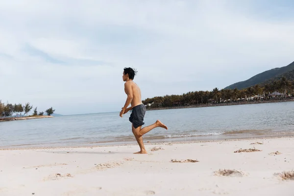 アクティブなアジア人男性 ビーチランニングを楽しむ 活気のある夕日を背景に砂で筋肉運動選手のトレーニング — ストック写真