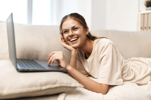 Smiling woman working on laptop in cozy home office, surrounded by modern technology and comfortable lifestyle.