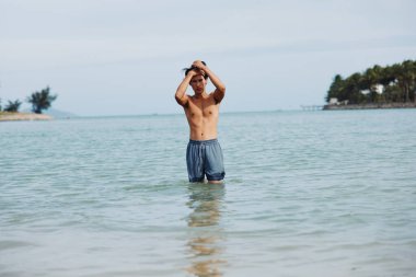 Gülümseyen Asyalı Adam Tropikal bir sahil tatili sırasında el değmemiş Mavi Okyanus suyunda ferahlatıcı bir yüzüşten zevk alıyor.