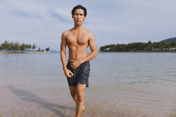 stock image Active Asian Athlete Running on the Beach: Fit, Muscular Man Exercising in the Sand, Enjoying the Freedom of Outdoor Cardio Workouts.