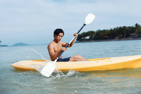 トロピカルビーチでハッピーなアジア人男性カヤック ターコイズオーシャンでカヌーでアクティブな夏休みを楽しむ — ストック写真