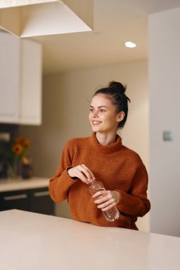 Neşeli genç bir kadın evde sağlıklı bir kahvaltıdan zevk alıyor, akıllı telefonunu gülümseyerek kullanıyor..