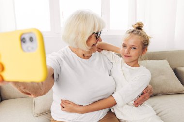 Beyaz bağ kuran torun fotoğrafçılık eğitimi çocuk aile fotoğrafı büyükanne videosu iki kopya mutluluk kanepesini arıyor birlikte gülümseyen selfie tişörtü kapalı alanda kucaklaşan telefon.