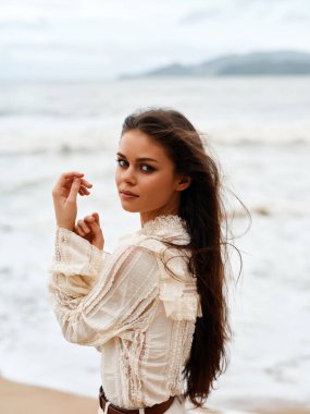 İfade Eden Güzel: Uzun siyah saçlı çekici bir kadın, Stüdyo Rock 'ta yalnız poz veriyor, Muhteşem Mavi Deniz ve Günbatımına bakıyor.