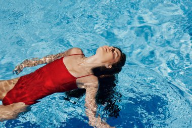 Kırmızı mayo içinde yüzen, uzun saçlı, güneş kremli cilt koruması olan, tatilde rahatlama konsepti olan mutlu bir kadın. Yüksek kalite fotoğraf