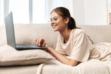 Oturma odasında dizüstü bilgisayarla çalışan gülümseyen bir kadın.