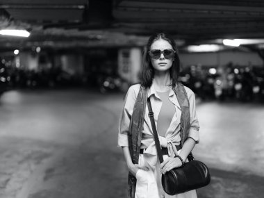 Şık bir genç kadın, çekici güzelliği olan modaya uygun bir model, şehir dışında, modern bir arka planda poz veriyor..