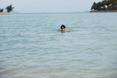 Yüzmek, Rahatlamak ve Tropikal Güzelliğin Tadını Çıkarmak: Mutlu Asyalı Bir Adam Mavi Okyanus Suyunda Arkadaşlarıyla Yaz Tatilinde Eğleniyor