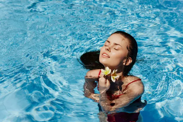 Yüzme havuzunda yüzen, kırmızı mayolu, güzel gülüşlü ve havuzda yüzen Bali çiçekli genç bir kadın. Tatilde rahatlama kavramı. Yüksek kalite fotoğraf