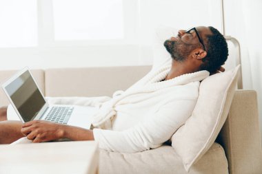 Bornozlu gülümseyen Afrikalı Amerikalı Modern İçişleri Bakanlığı 'nda dizüstü bilgisayarda çalışıyor ya da Genç Afrikalı Amerikalı Freelancer Sabah Işığı' nda koltukta dinlenirken dizüstü bilgisayarında yazıyor.