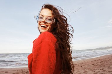 Gülümseyen Kadın Özgürlüğün tadını çıkarıyor: Renkli güneş gözlüklü güzel bir kadının portresi, Günbatımında bir sahilde tasasız bir yaşam tarzını kucaklıyor.