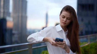 Sokakta elinde telefonla gezen bir kadın öğleden sonra gökdelenlere bakan bir arka planda yaşayan bir iş kadını ve serbest çalışan bir turist. Yüksek kalite 4k görüntü