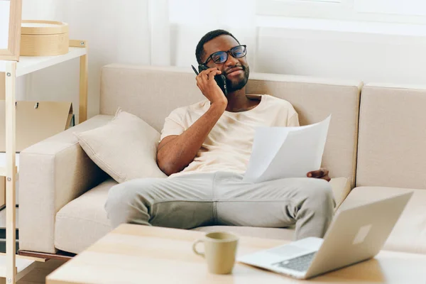 Усміхнений Афроамериканський Чоловік Працює Ноутбуці Сучасній Вітальні Розмовляючи Телефону — стокове фото