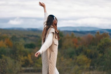 Dağ manzarasında dans eden, kulaklıkla müzik ve özgürlüğün tadını çıkaran kadın.