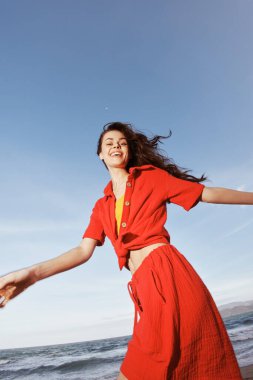 Sahilde esen yaz esintisinde dans eden neşeli kadın özgürlük ve mutlulukla gülümsüyor.