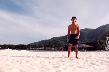 Sahili kucaklayan güçlü Asyalı atlet: Kum üzerinde sağlıklı bir yaşam tarzında koşan adam