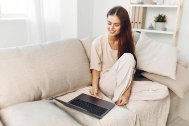 Oturma odasında dizüstü bilgisayarda çalışan gülümseyen kadın.