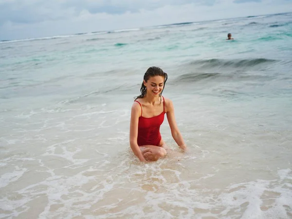 Sexy female model in red swimsuit with athletic body stands in the water in the ocean and poses, body maintenance on vacation. High quality photo